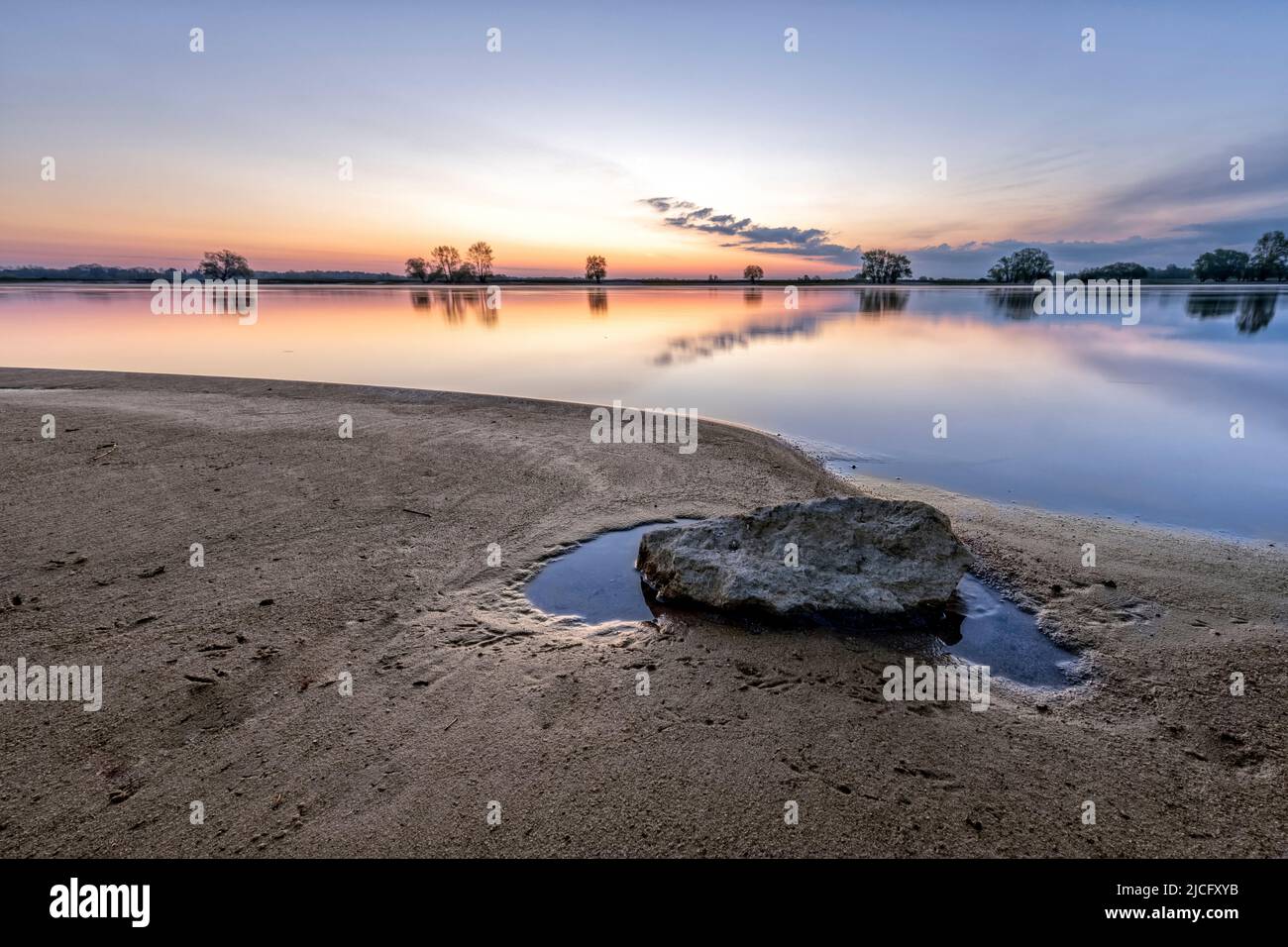 The Elbe with a reflection and a stone on the beach at sunrise Stock Photo