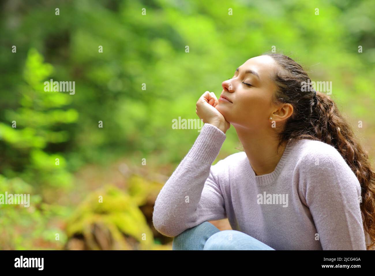 Relaxed woman sitting with closed eyes breathing fresh air in a beautiful green forest Stock Photo