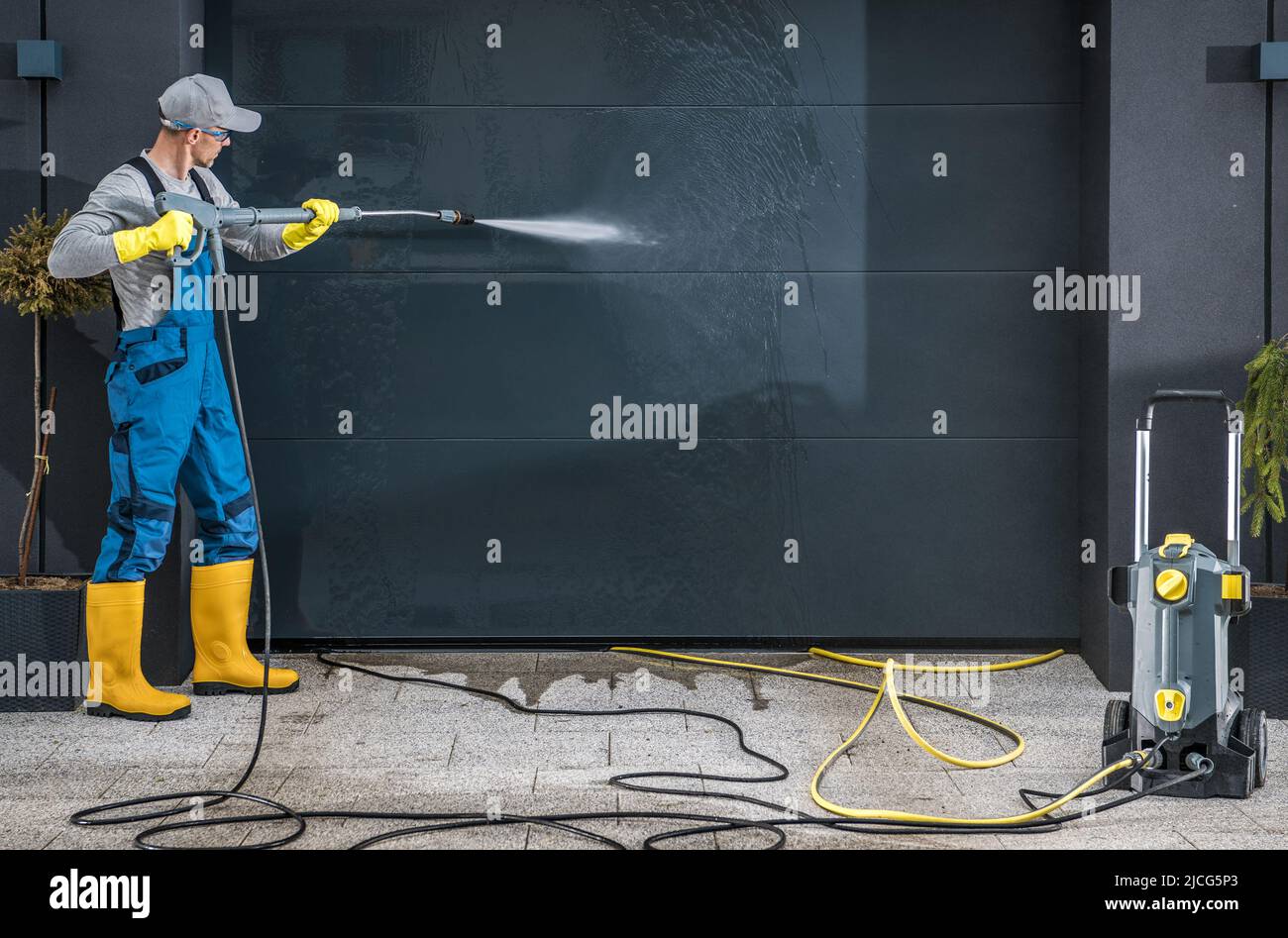 Caucasian Men in His 40s Powerful Pressure Washing Residential Garage Doors. Using Pressurized Water Jet to Clean Heavy Dirt. Stock Photo