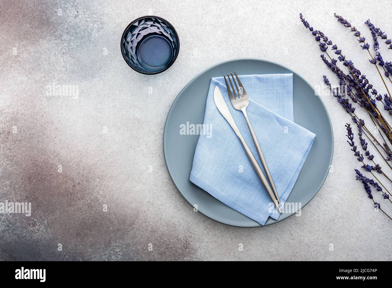 Table setting, empty plate with napkin and cutlery on a gray-pink concrete background, top view of the served table decorated with lavender flowers Stock Photo