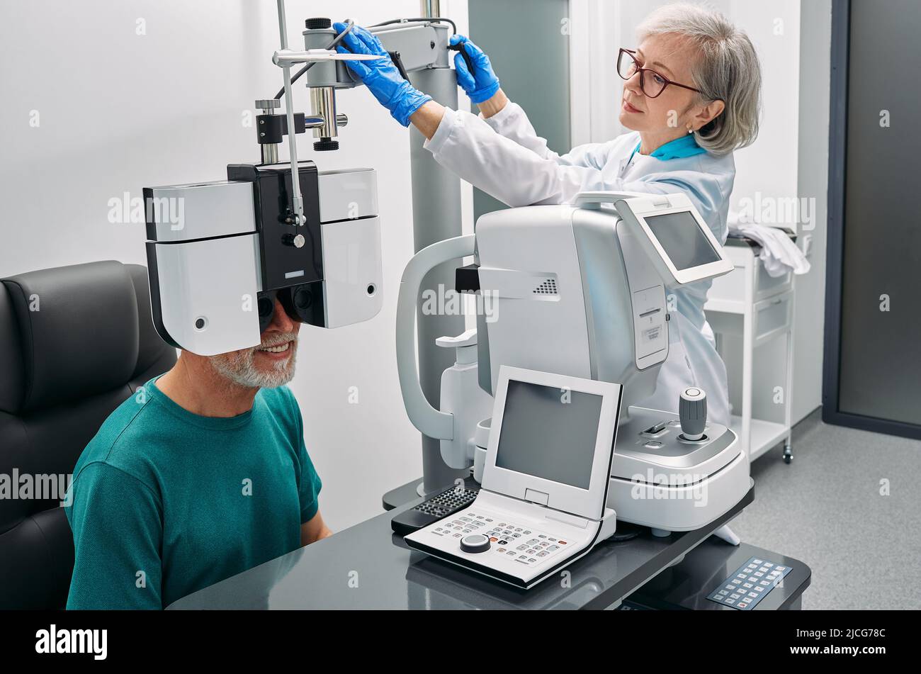 Optometrist doing eyesight test for senior patient using modern phoropter at ophthalmology clinic. Eye exam and vision diagnostic Stock Photo
