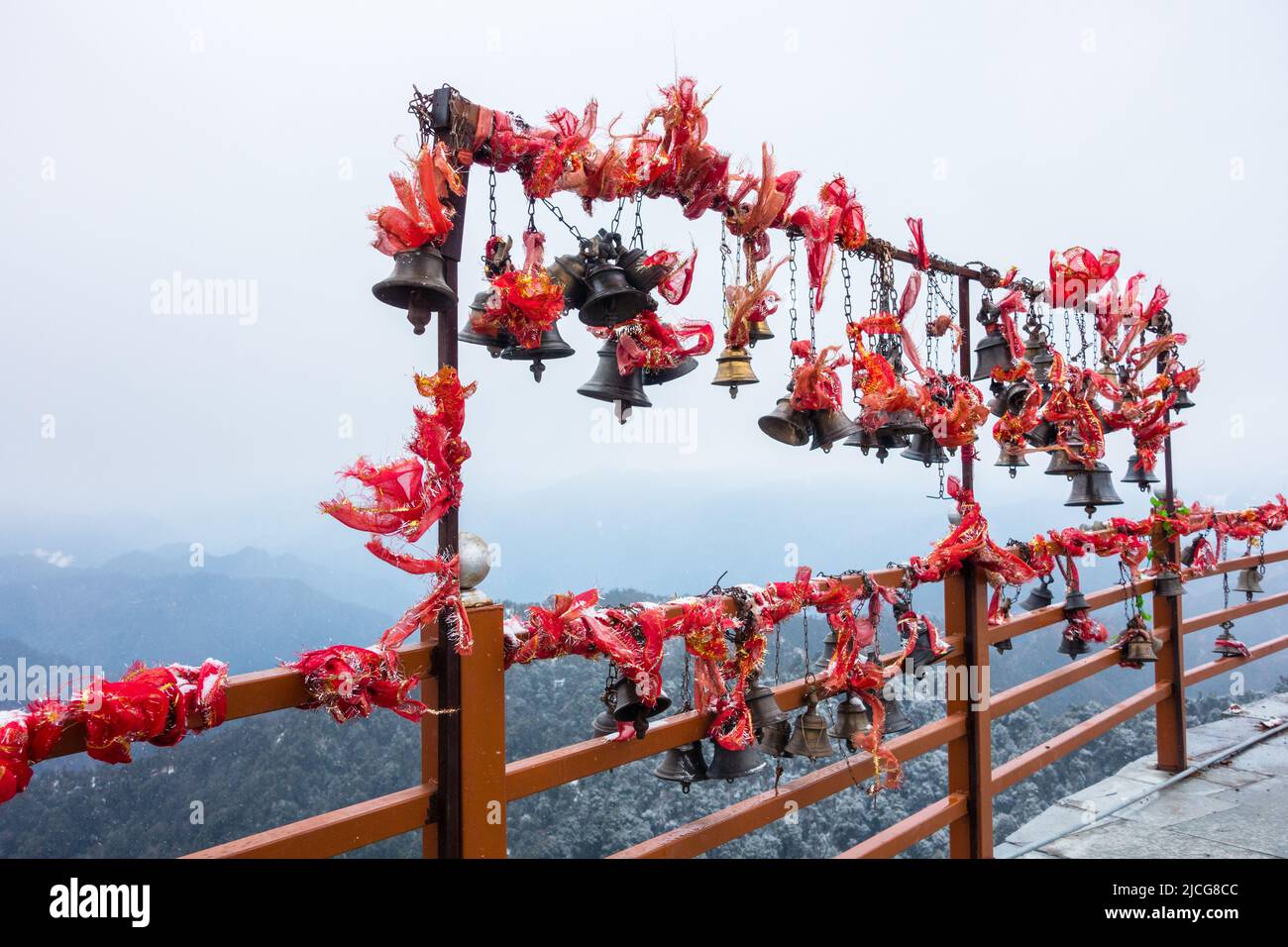 A wide angle shot of hanging bells with holy red cloths with a snow covered mountains in the Background, Kartik Swami Temple, Rudraprayag Uttarakhand Stock Photo