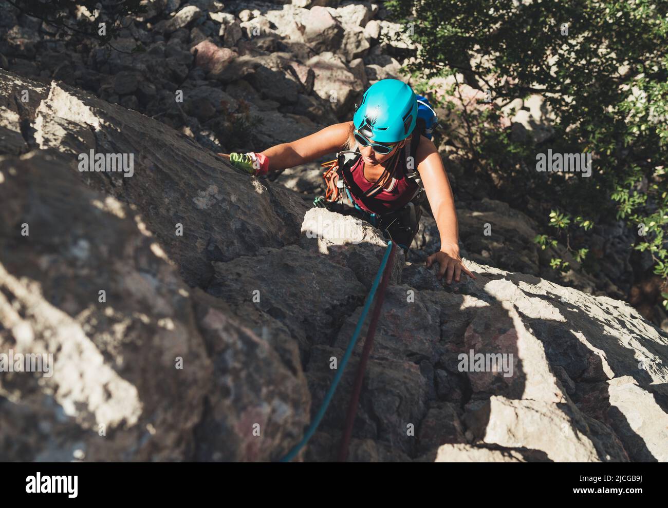 Active Woman in protective helmet and sunglasses on cliff rock wall lead climbing using rope and climbing harness in Paklenica National park, Croatia. Stock Photo