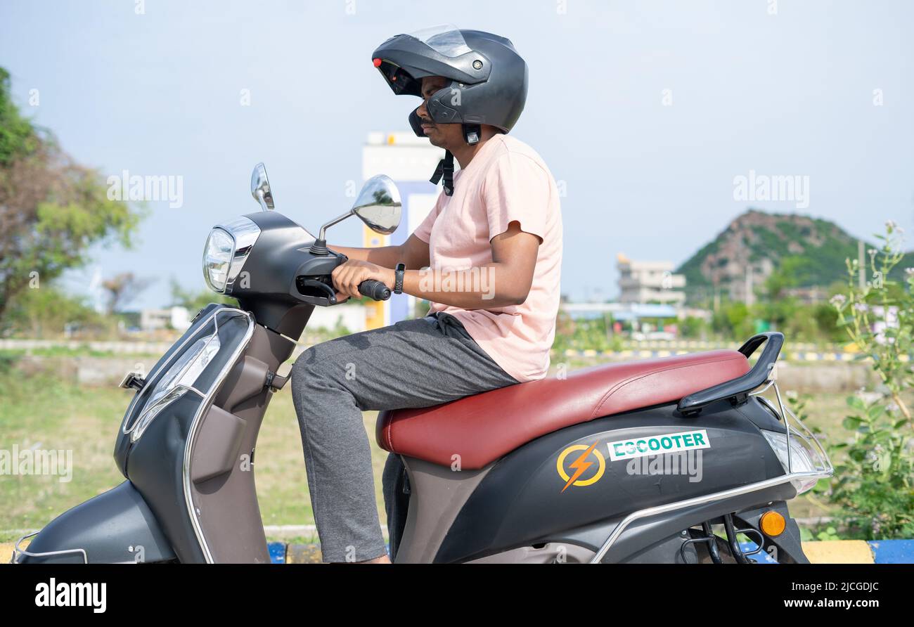 Man driving Ev or electric scooter by wearing helmet on road - concept of safety, technology and lifestyle. Stock Photo