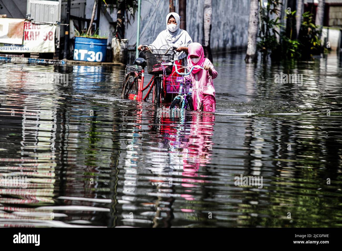 Sidoarjo, Indonesia. 13th June, 2022. A mother and her daughter push their bikes through flood water after heavy rain at Waru in Sidoarjo, East Java, Indonesia, June 13, 2022. Credit: Kurniawan/Xinhua/Alamy Live News Stock Photo