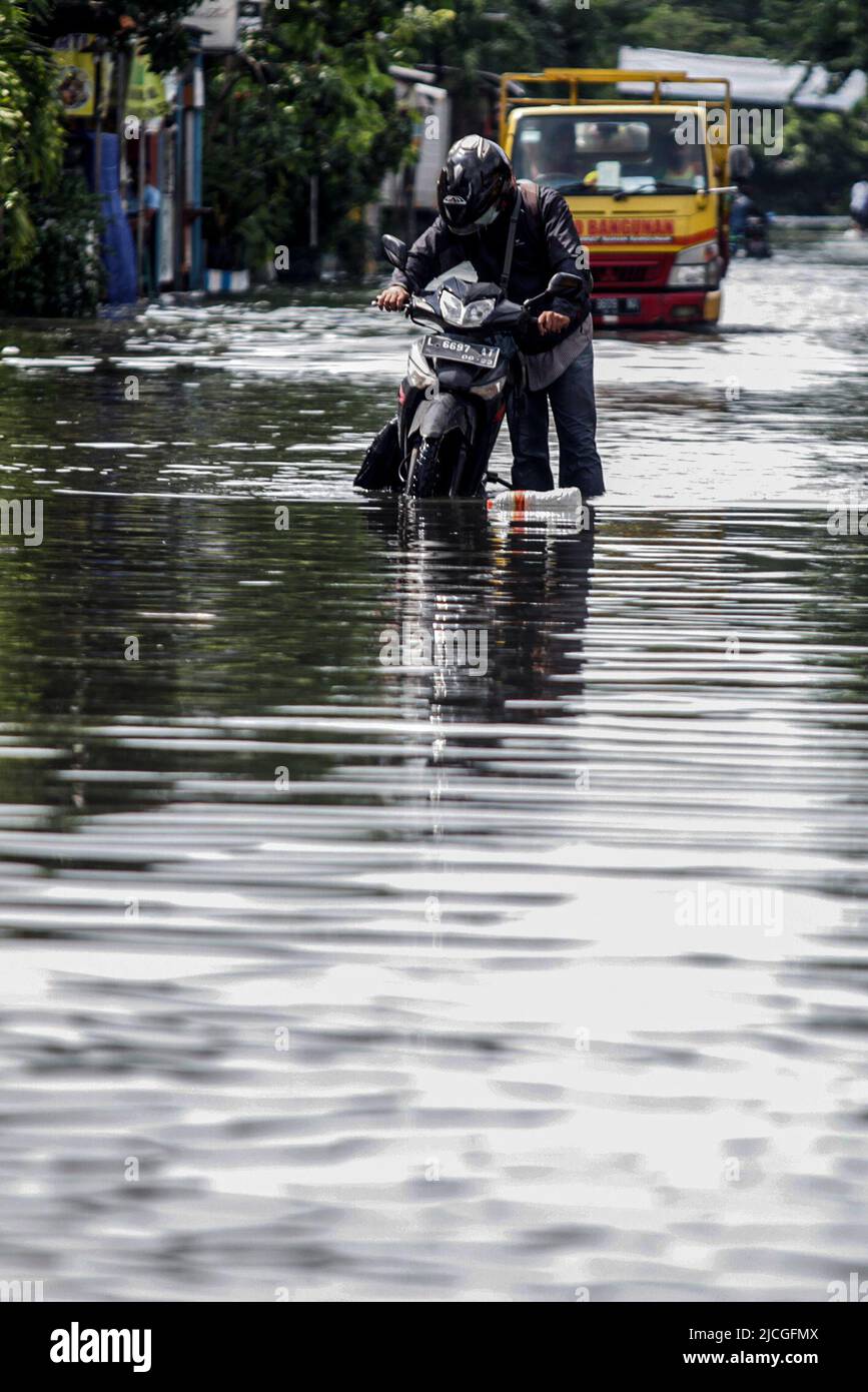 Sidoarjo, Indonesia. 13th June, 2022. A man walks with his motorbike through flood water after heavy rain at Waru in Sidoarjo, East Java, Indonesia, June 13, 2022. Credit: Kurniawan/Xinhua/Alamy Live News Stock Photo