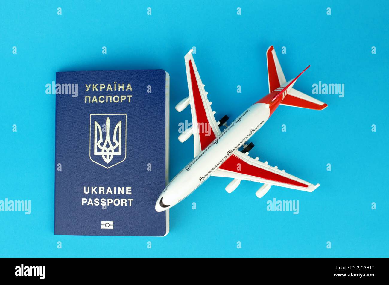 Ukrainian biometric passport and toy plastic plane on a blue background. Departure of Ukrainians abroad. Stock Photo