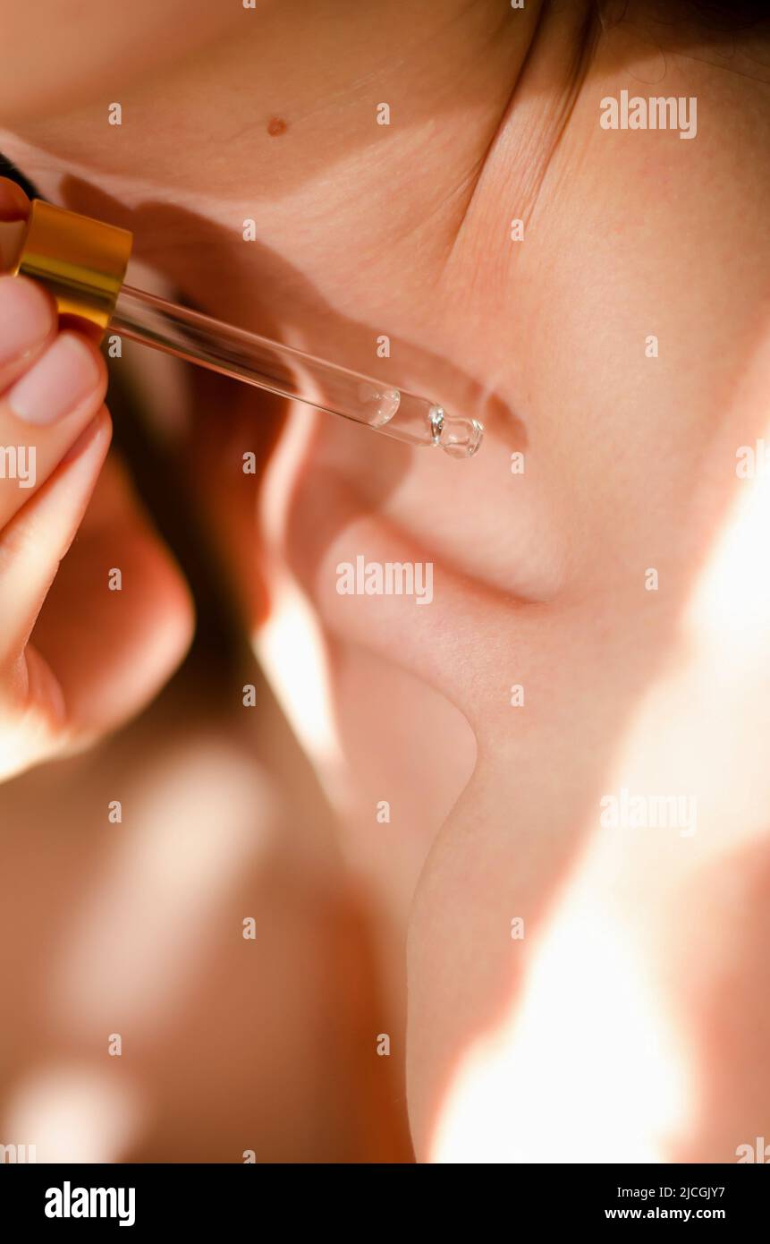 A woman applies oil to body. A drop of essential oil drips from a pipette onto a woman's collarbone. Serum for the body. Cosmetic procedures Stock Photo