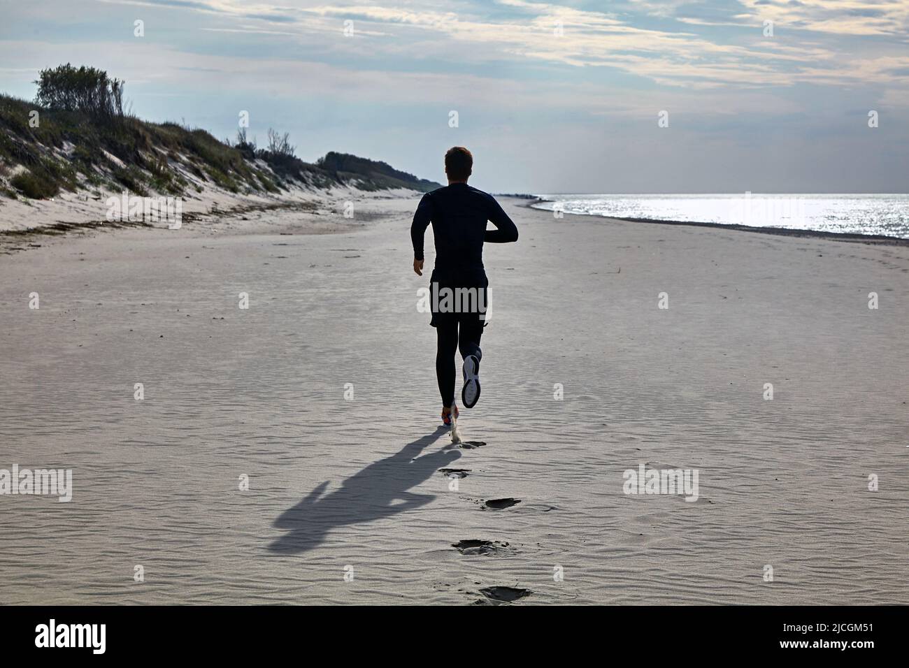 A young man in black sports gear and orange sneakers is jogging on the
