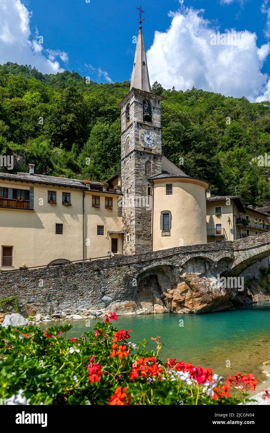 Old church with spire as mountain river flow under stone bridge in small town of Fontainemore in Aosta Valley, Italy. Stock Photo