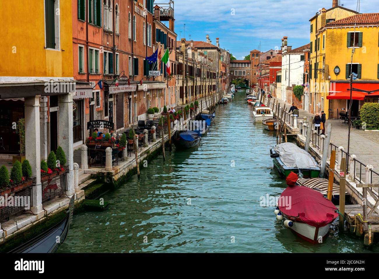 View of boats on narrow canal along old colorful houses and typical street in Venice, Italy. Stock Photo