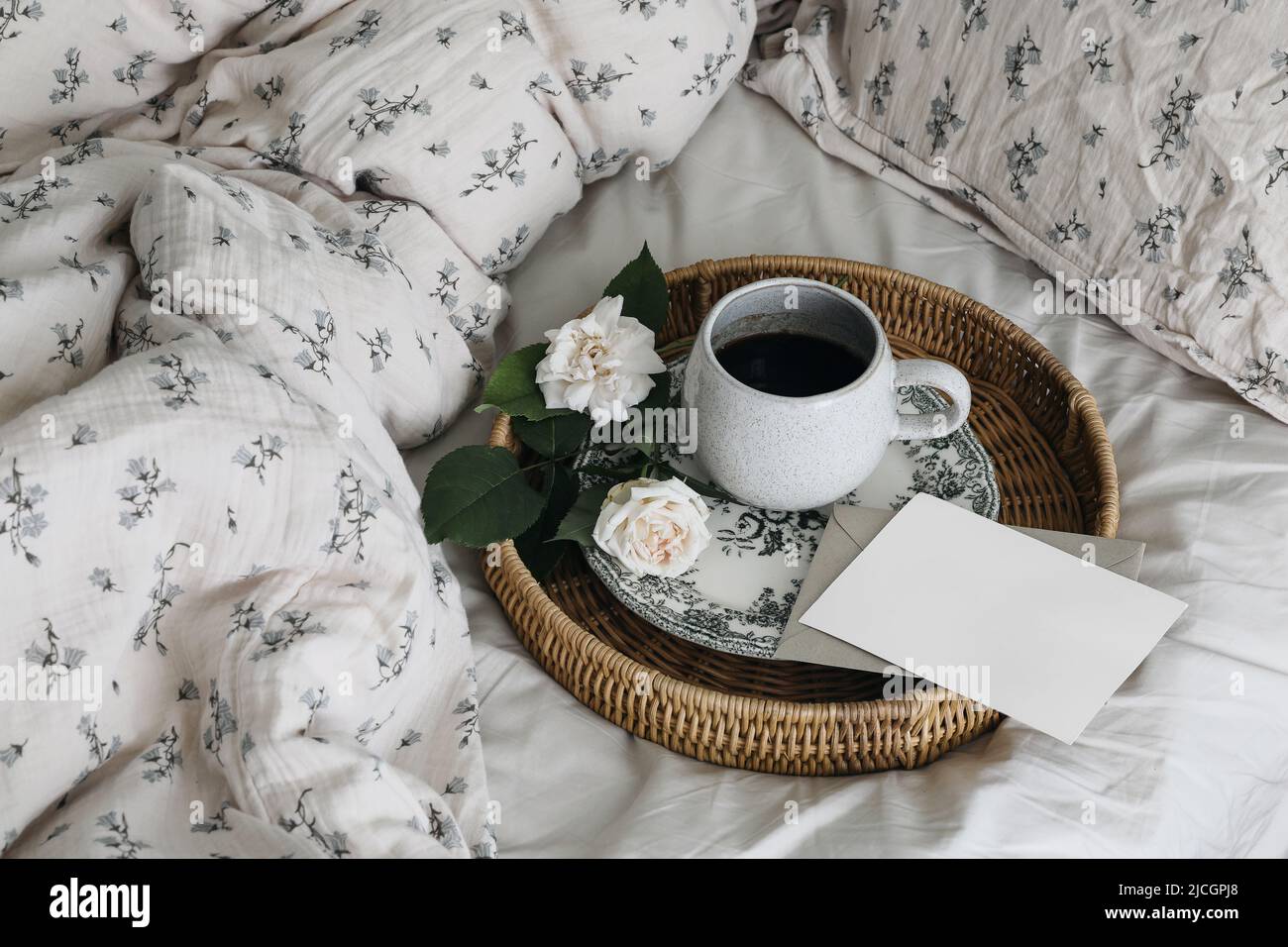 Rustic vintage breakfast in bed composition. Cup of coffee, rose flowers on porcelain plate. Wicker tray. Blank greeting card, invitation mockup Stock Photo