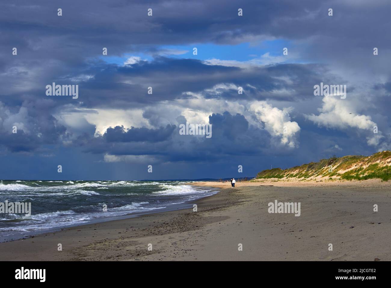 Blue dramatic clouds and sunbeams break through over the sea beach ...