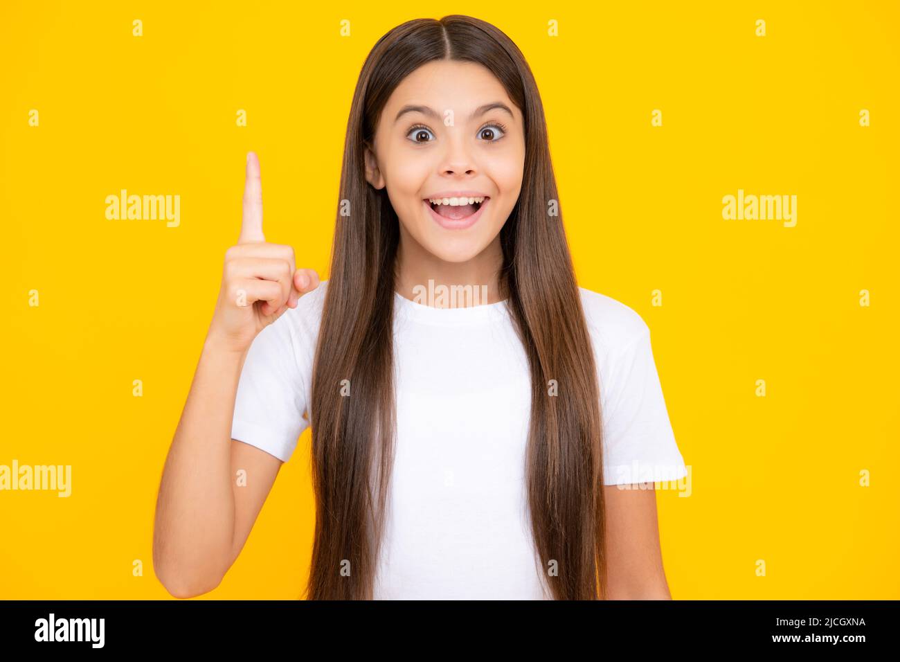 Happy teenager portrait. Funny face of young teenager pointing up with finger, isolated on yellow background. Girl has great new idea. Funny school Stock Photo