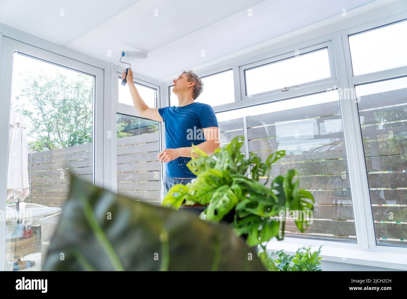Young man painting the plastic ceiling of the conservatory in white color by the roller. DIY, Do