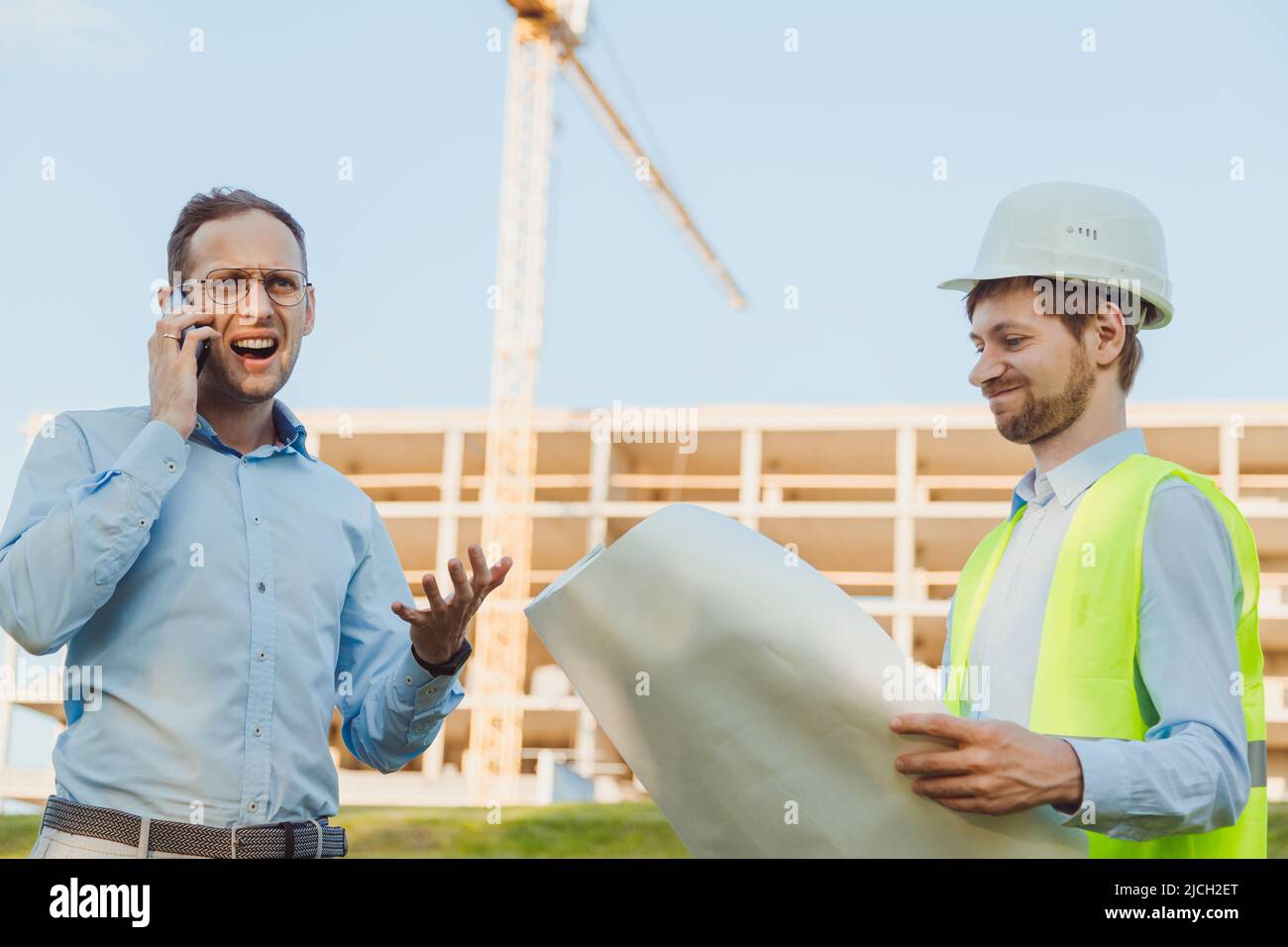 Angry emotionally unrestrained customer shouting on phone at construction site standing with chief engineer. Delay concept in construction. Emotions a Stock Photo