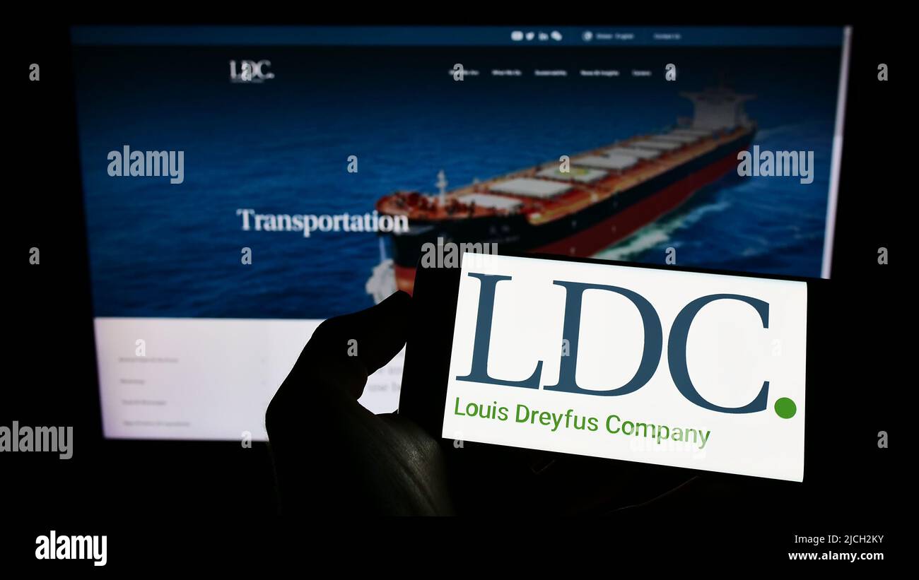 Person holding cellphone with logo of Louis Dreyfus Company BV (LDC) on screen in front of business webpage. Focus on phone display. Stock Photo