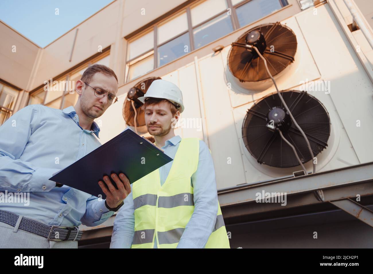 Service engineers in uniform inspecting industrial refrigeration system, outdoor refrigeration
