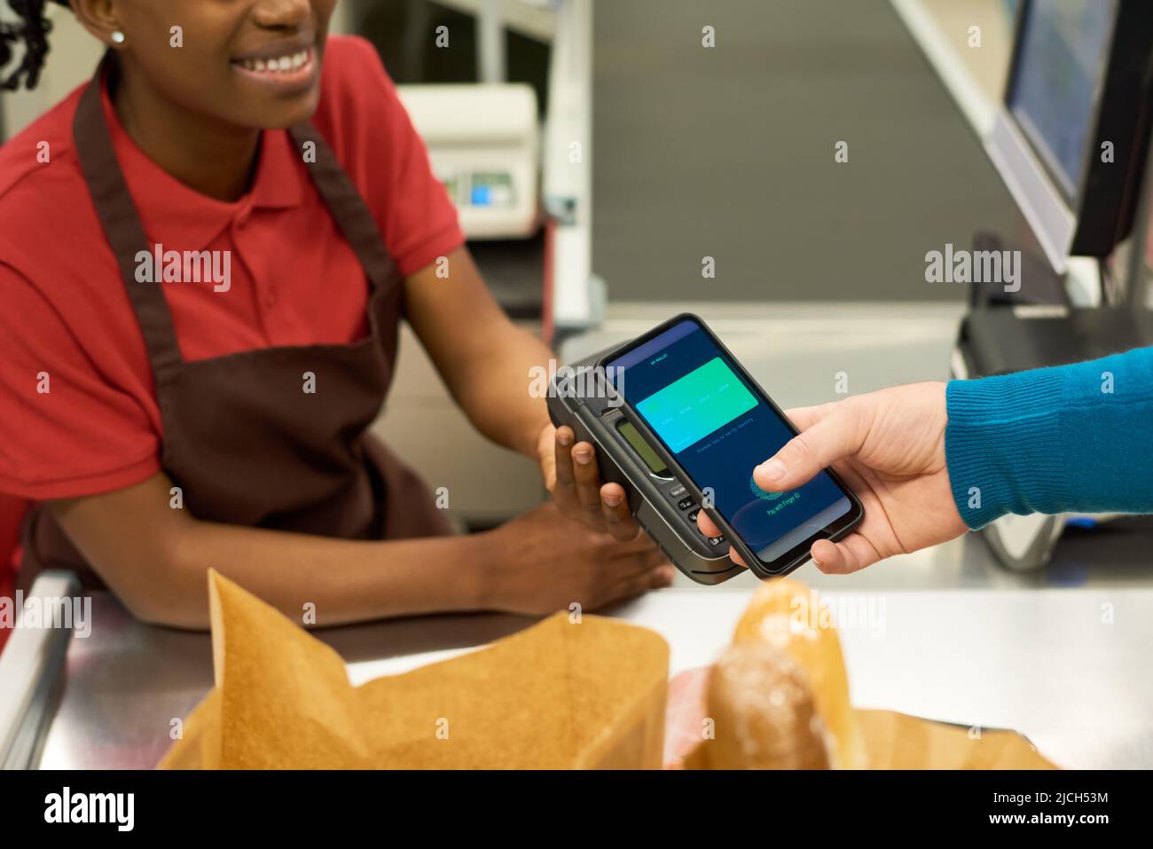 Hand of consumer with smartphone paying for food products by contactless payment while standing by counter in supermarket Stock Photo