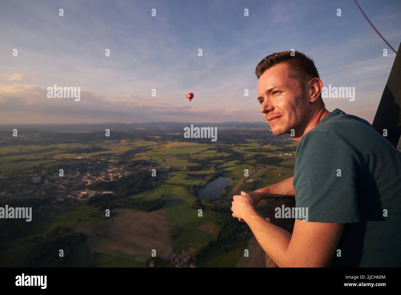 Man enjoying from view from hot air balloon during flight over beautiful landscape at sunset. Themes adventure, freedom and travel. Stock Photo