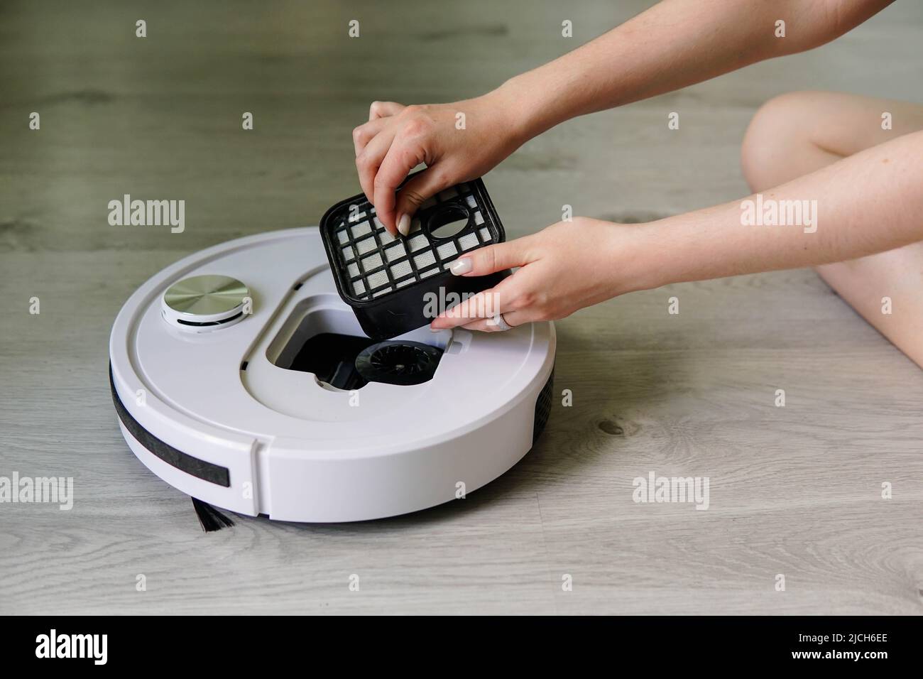 Young woman taking out container and filter of automatic robot vacuum cleaner to clean it from dirt and debris. Smart home technology. Stock Photo