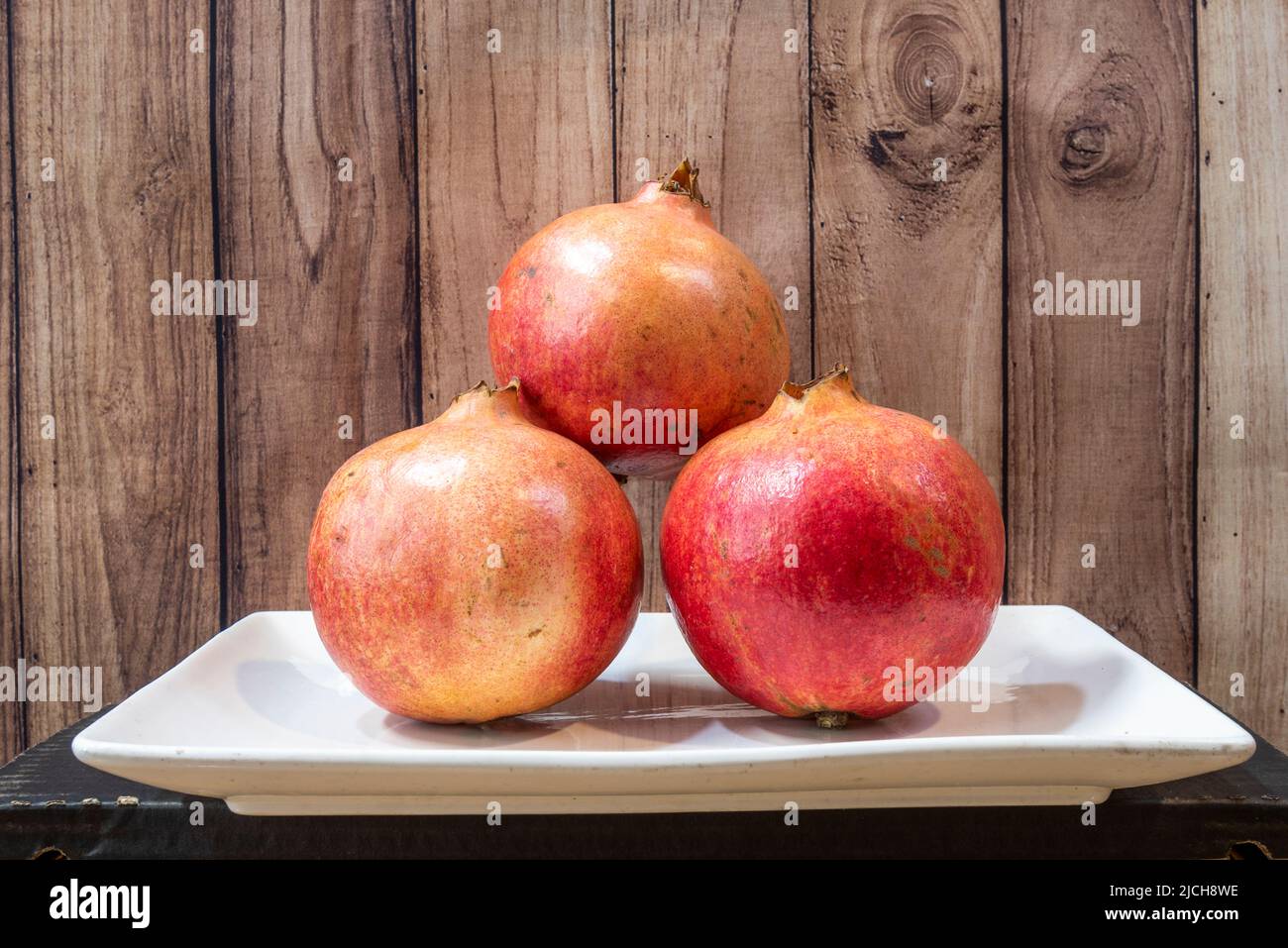 Plate with trio of ripe pomegranates and dark wooden background Stock Photo