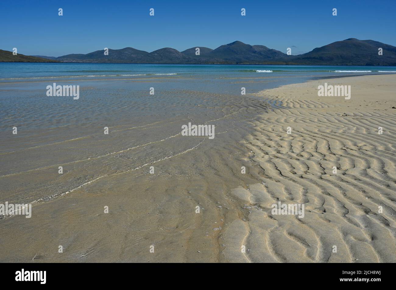 Luskentyre beach, Isle of Harris. Blue sky, mountains in background, sea and wavy lines of sand in foreground. No people. Tranquil, summer scene. Stock Photo