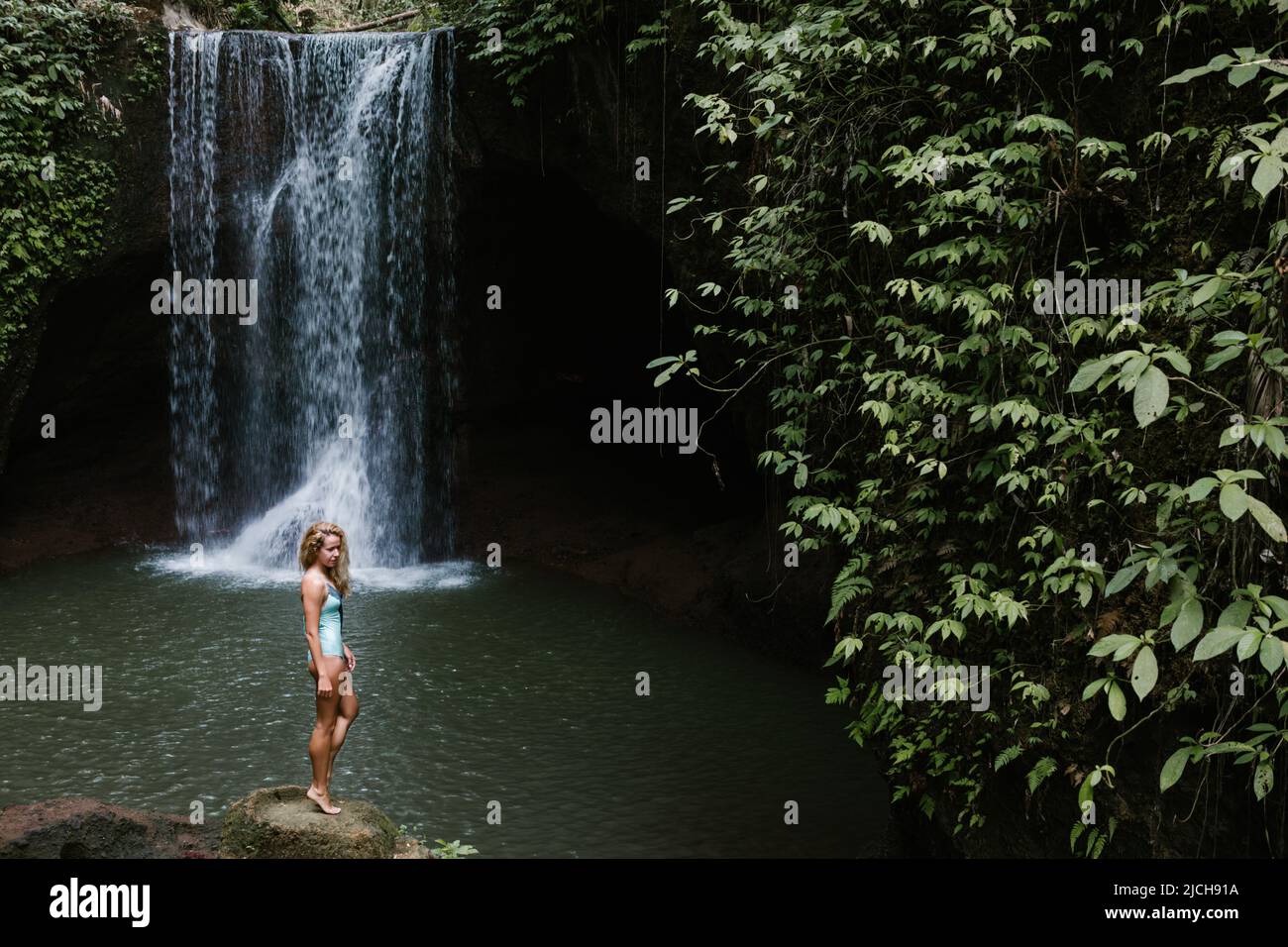 Woman stand and look at pool under falling water of Suwat waterfall in tropical jungle. Nature day tour, hiking activity adventure and fun Stock Photo