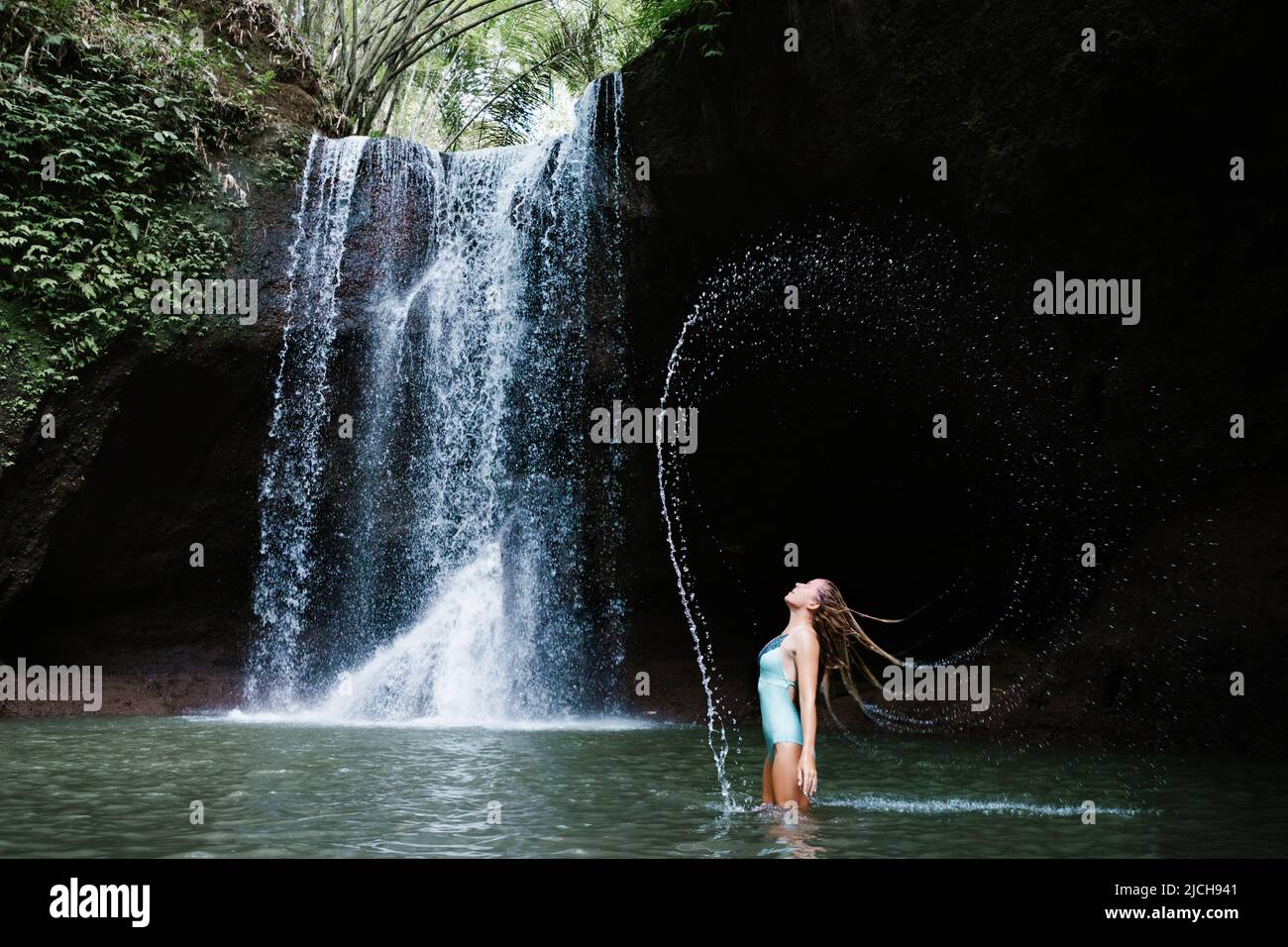 Woman have fun in natural pool under falling water of Suwat waterfall in tropical jungle. Nature day tour, hiking activity adventure and fun at family Stock Photo