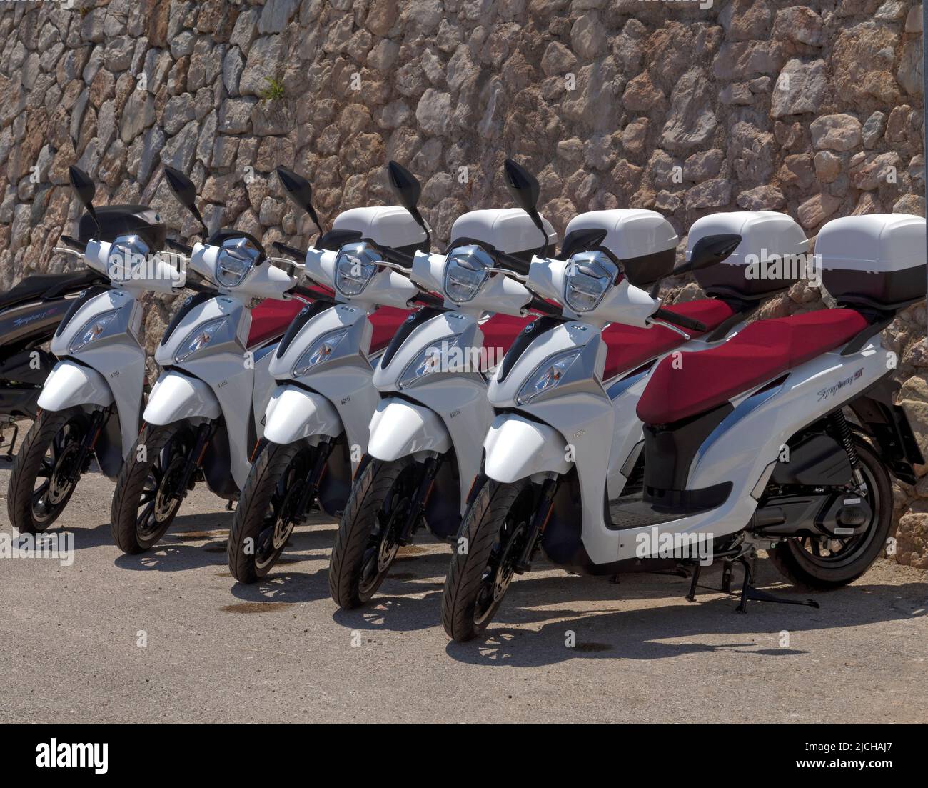 A regimented row of motor bikes / scooters for hire, Tilos island Dodecanese, near Rhodes Greece Stock Photo