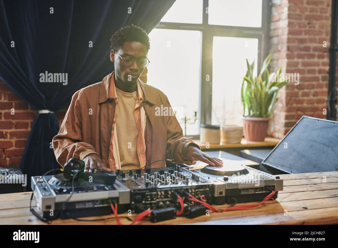 Young serious black man looking at dj board while adjustic musical equipment and touching turntables before performing Stock Photo