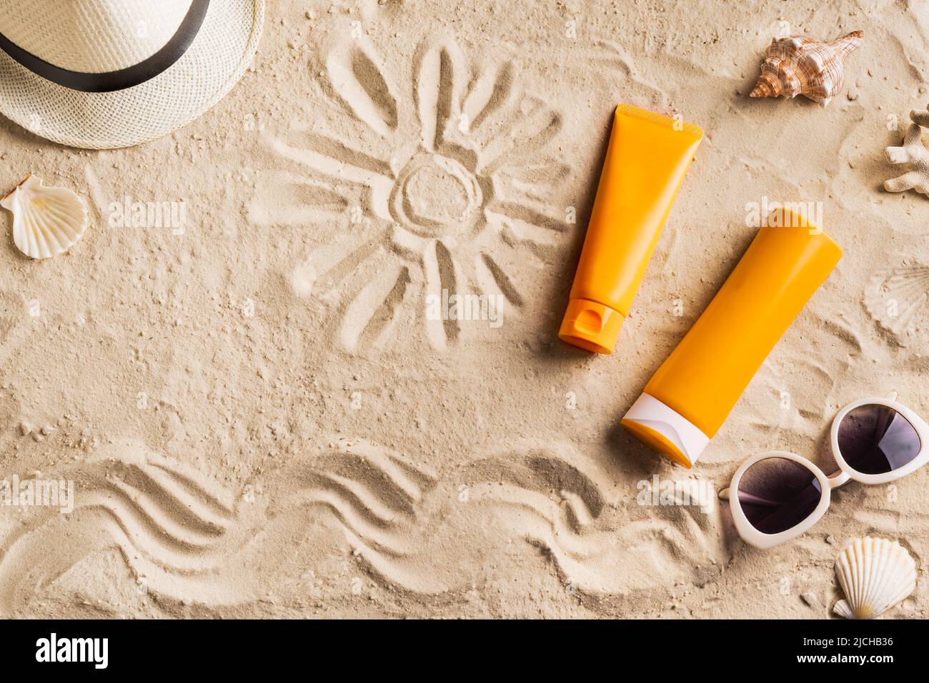 Summer travel beach flat lay composition, copy space. Hat, sunglasses, sunscreen lotion, sunblock cream and seashells on beach sand background. Summer Stock Photo