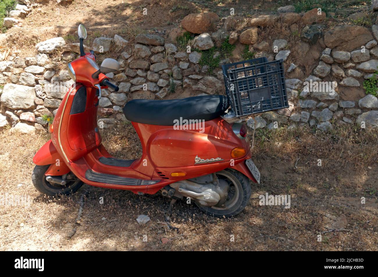 Orange Vespa scooter parked near a dry stone wall by the roadside,, Tilos island Dodecanese, near Rhodes Greece Stock Photo