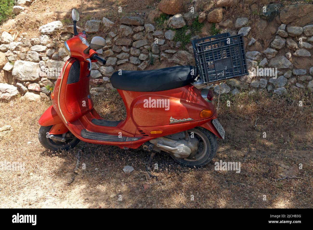 Orange Vespa scooter parked near a dry stone wall by the roadside,, Tilos island Dodecanese, near Rhodes Greece Stock Photo