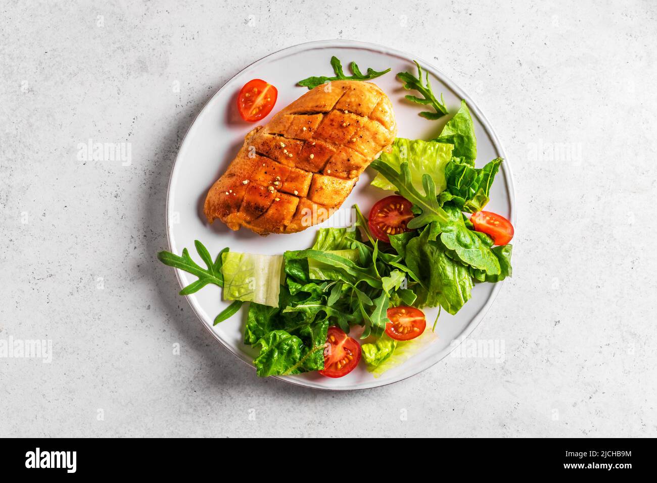 Chicken Salad with fresh vegetables and greens on white table. Roasted Chicken Fillet, green lettuce, arugula, tomatoes salad for healthy lunch, top v Stock Photo