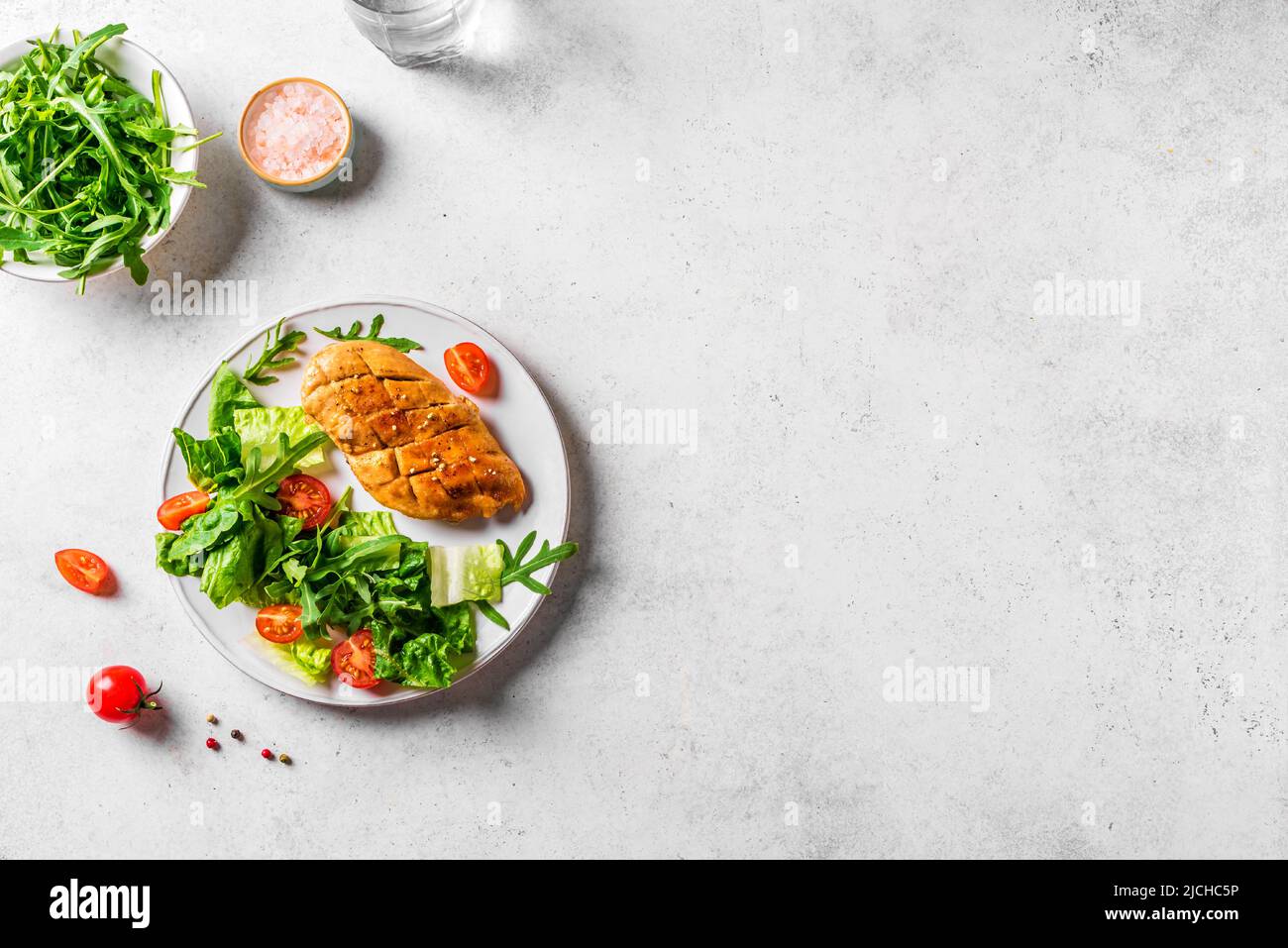 Grilled Chicken Salad with fresh vegetables and greens on white table. Roasted Chicken Breast, green lettuce, arugula, tomatoes salad for healthy lunc Stock Photo