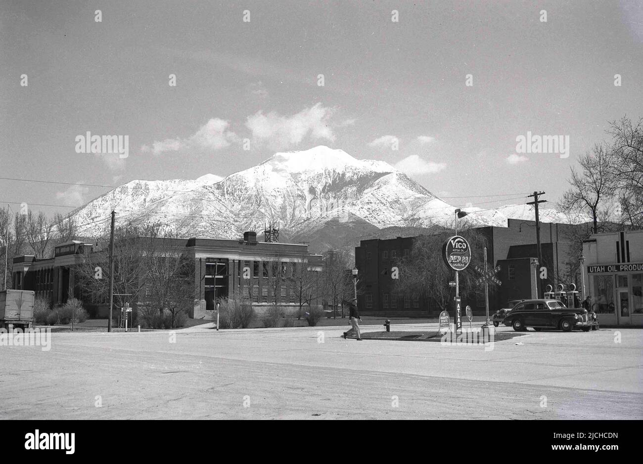 1930s, historical, a car of the era at at a gas station, Utah, USA, with the famous snow covered Wasatch mountains in the distance. A Rail road Crossing sign is on the forecourt, while the name Utah Oil Products is on the garage building. On the station sign the names Vico Motor Oil and Pep 88 gasoline, the oil and gas brands of the Utah Oil Refining Company. The first oil refinery in Utah, established in 1908, these brand names remained in use until 1948, when replaced by the brand name UTOCO. Other motor brands of the day seen; Atlas tyres & batteries & Quaker State motor oil. Stock Photo