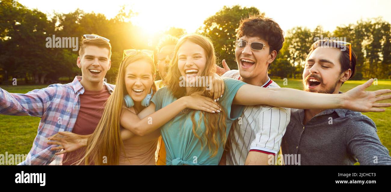 Group of six best friends have fun and laugh out loud while walking in park on summer sunny day. Stock Photo