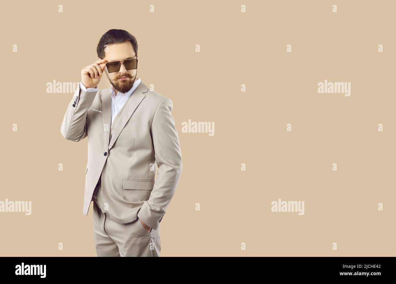 Business man in elegant suit and sunglasses posing on blank beige copy space background Stock Photo