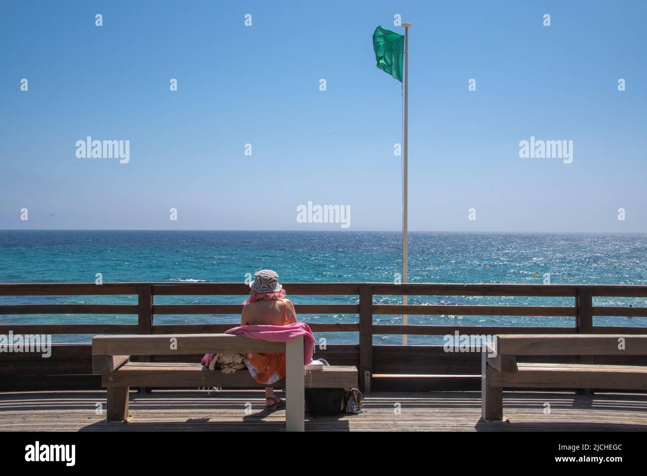 A women sitting on a bench looks out to sea at Gigaro Beach, Var, Provence-Alpes-Côte d'Azur, France. Stock Photo