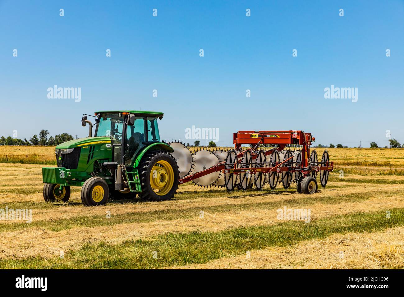 A John Deere tractor with a wheel rake attached in a field at the Merced National Wildlife refuge in the Central Valley of California USA Stock Photo