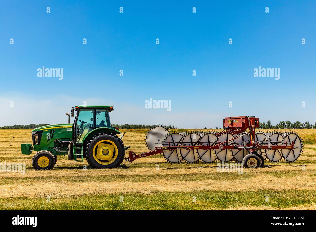 A John Deere tractor with a wheel rake attached in a field at the Merced National Wildlife refuge in the Central Valley of California USA Stock Photo