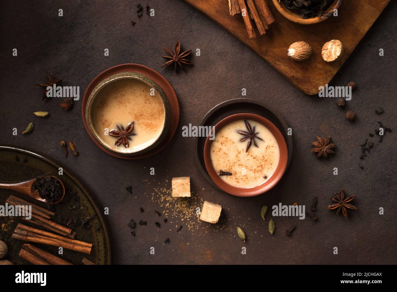 Masala Chai Tea in ceramic cup with ingredients. Traditional indian spicy black tea with milk on rustic dark background Stock Photo