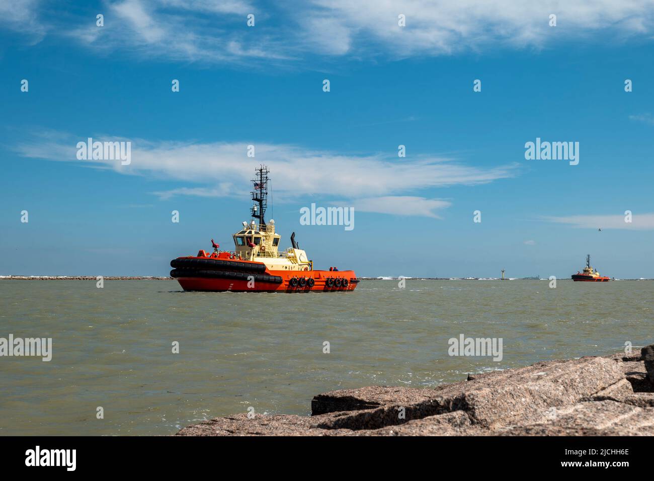 Two tugboats cruising in from sea in a shipping channel after guiding an oil tanker, on a sunny day with blue sky and a few clouds. Stock Photo
