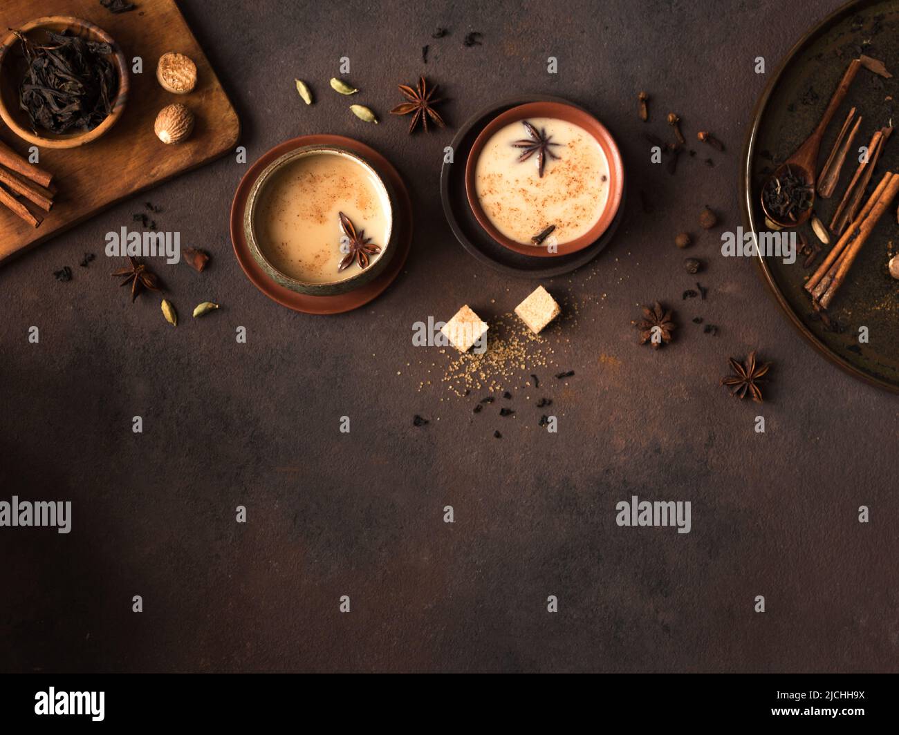 Masala Chai Tea in ceramic cup with ingredients. Traditional indian spicy black tea with milk on rustic dark background, copy space. Stock Photo