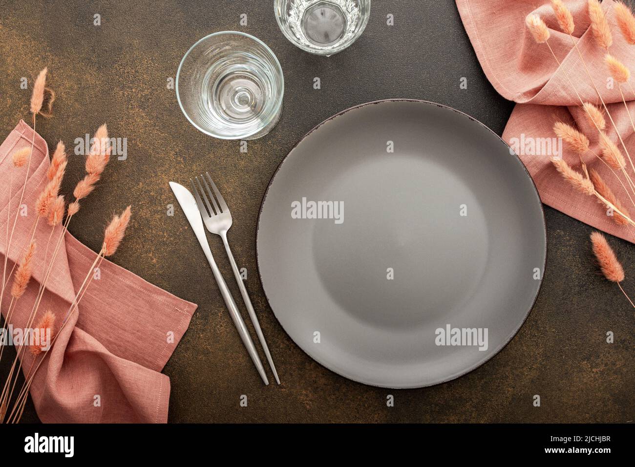 Table setting, empty gray plate with napkin and cutlery on a brown background, top view of the served table decorated with dry flowers Stock Photo
