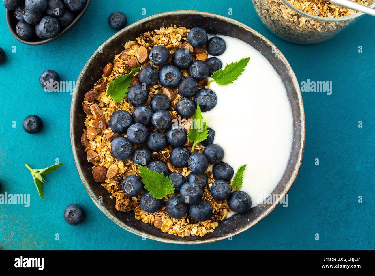Homemade granola with yogurt, blueberries and mint leaves in a bowl on a turquoise background, delicious healthy breakfast Stock Photo