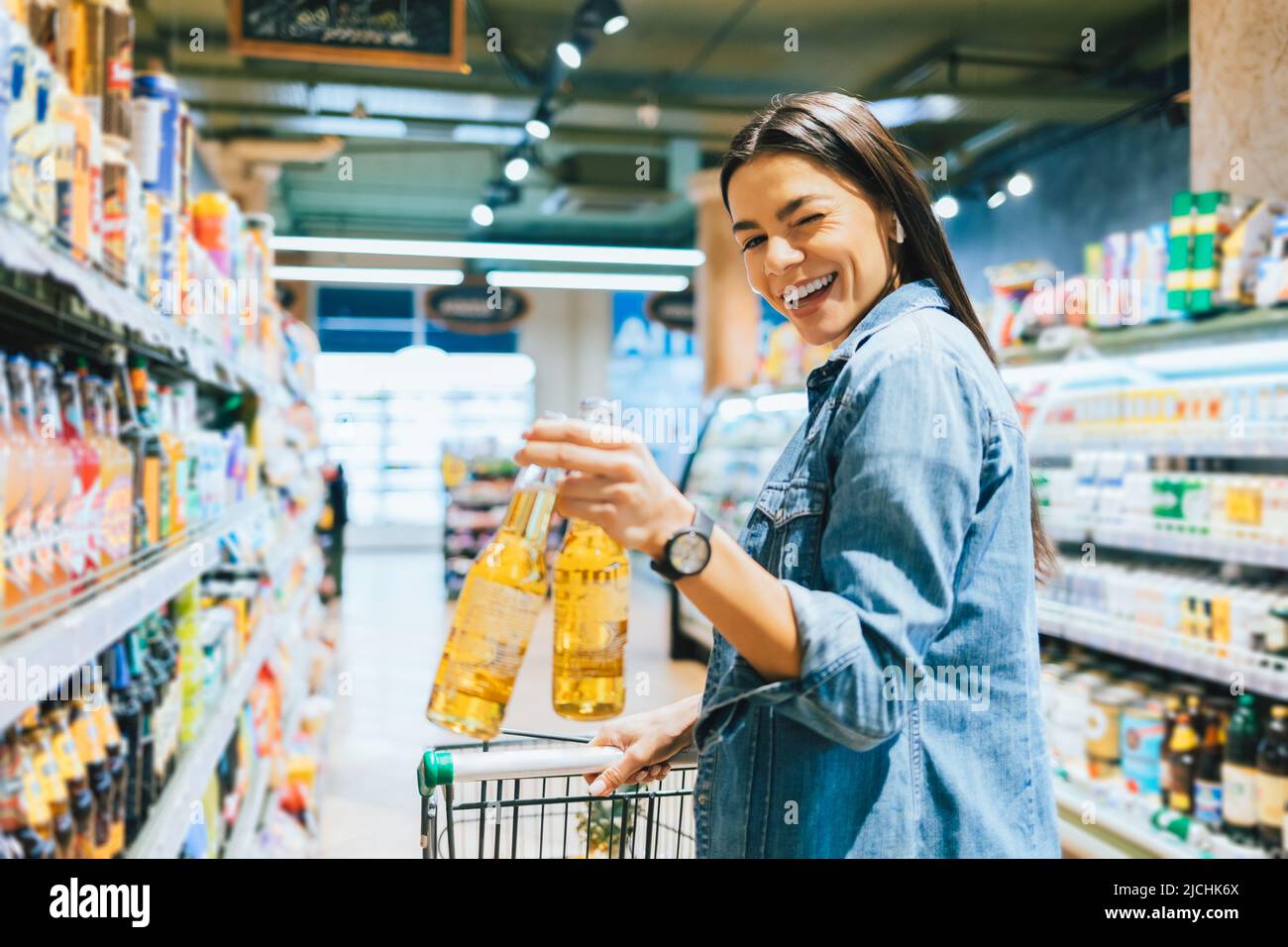 Portrait joyful young woman buying beer in liquor store holding two