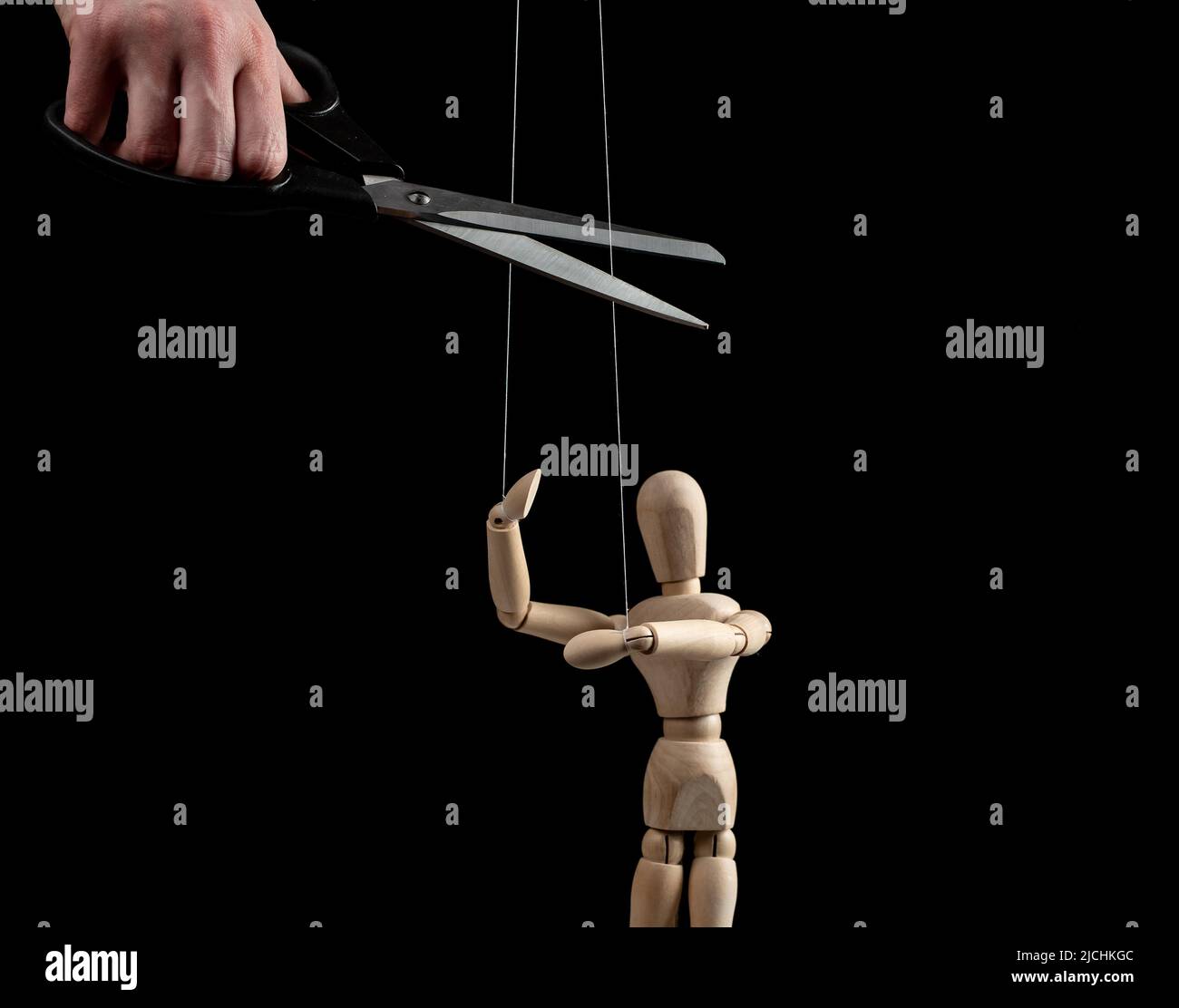 Hand with scissors cutting strings holding puppet. Independence, liberation from slavery, control, abuse cessation, successful recovery from addiction concept on black background. High quality photo Stock Photo