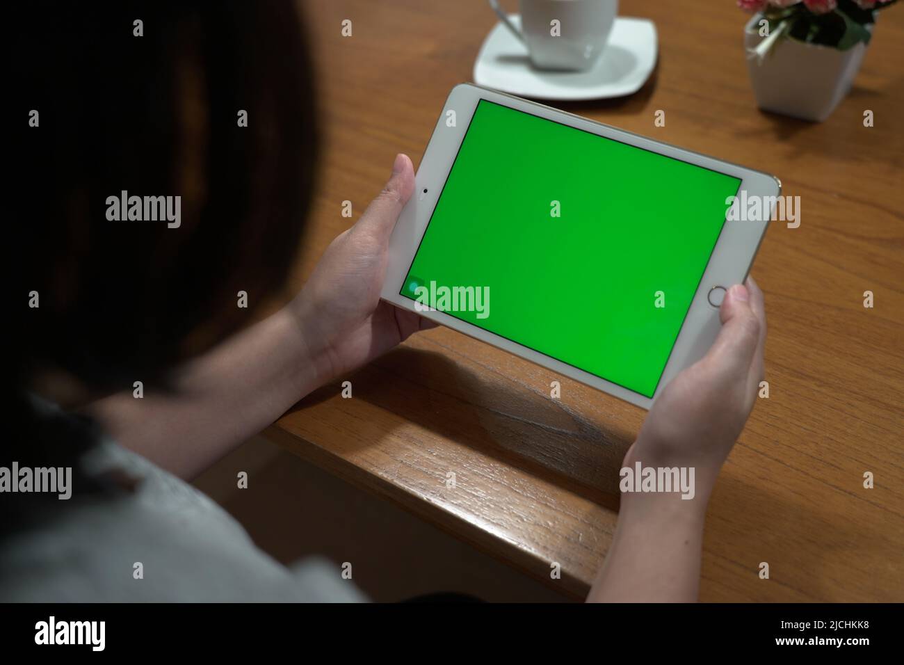 Woman using tablet with green screen mockup in living room view from behind the shoulder. Stock Photo
